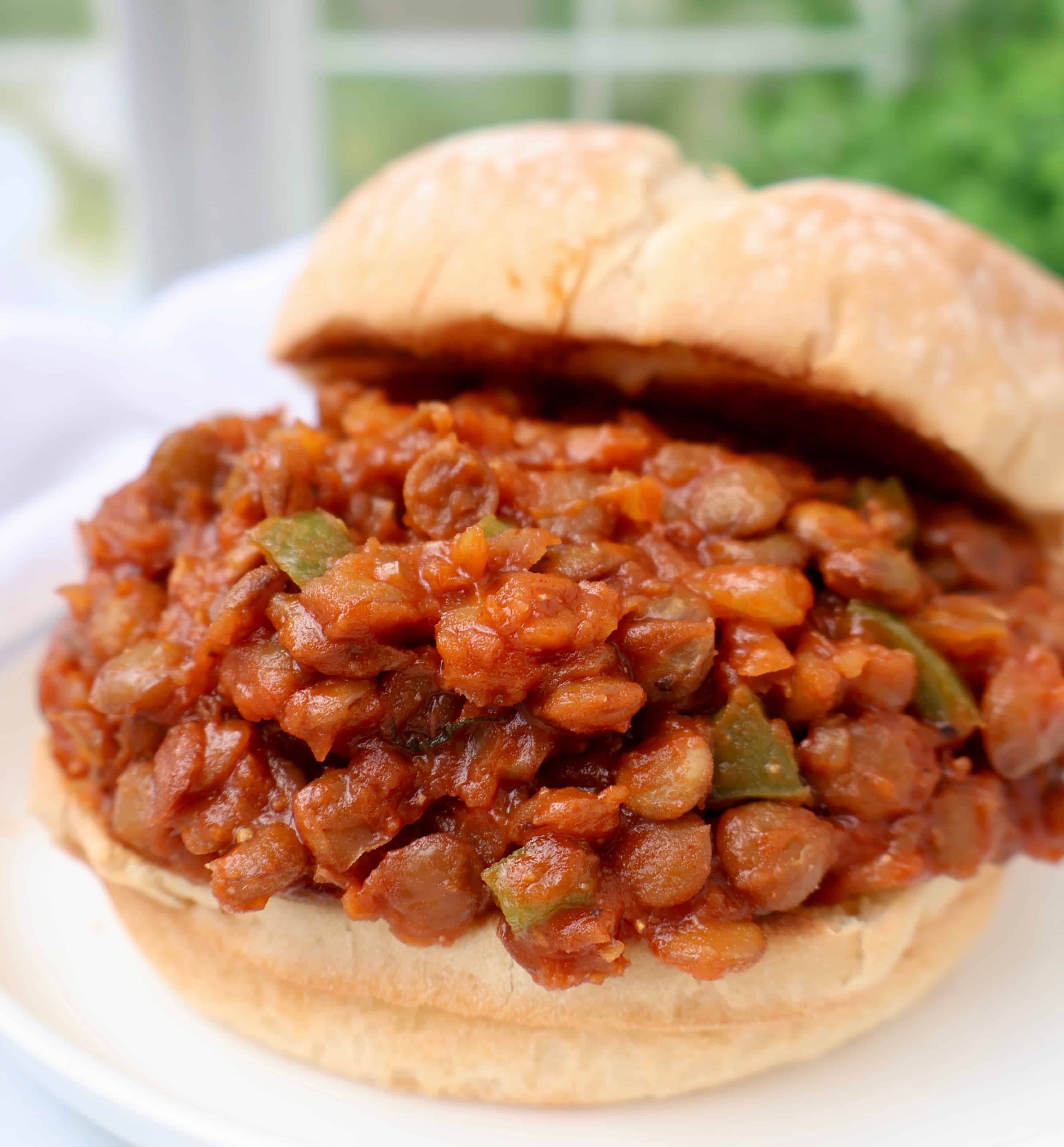 A close-up of a sandwich filled with a hearty lentil and vegetable mixture in a tomato-based sauce, served on a soft, round bun.