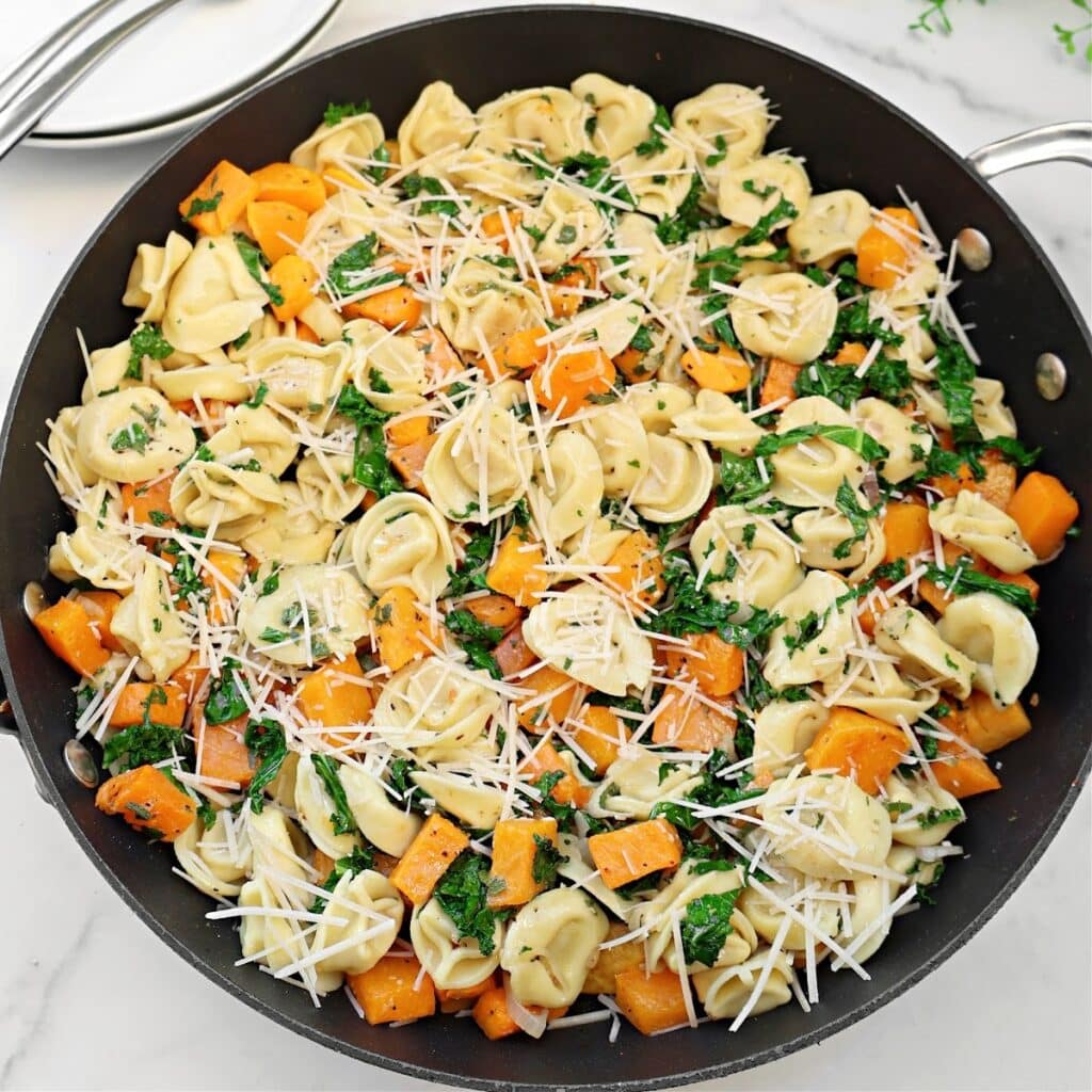 A skillet filled with tortellini with butternut squash, fresh spinach, and grated Parmesan cheese, all mixed together.