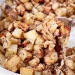 Close-up of roasted breakfast potatoes mixed with caramelized onions and herbs, served in a dish with a metal spoon. The crispy, golden brown potatoes look perfect for a hearty morning meal.
