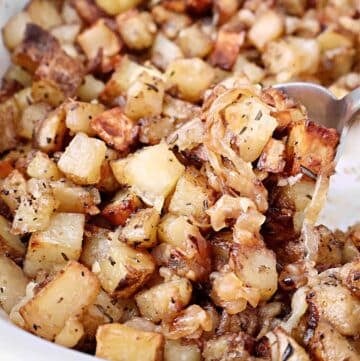 Crispy Roasted Breakfast Potatoes Close-up of roasted breakfast potatoes mixed with caramelized onions and herbs, served in a dish with a metal spoon. The crispy, golden brown potatoes look perfect for a hearty morning meal.