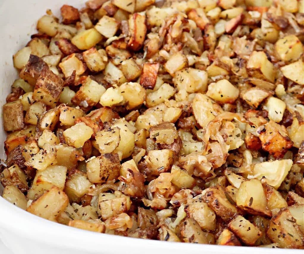 Close-up of roasted breakfast potatoes, diced and mixed with spices and herbs for a golden-brown, crispy texture. The flavorful potatoes are served in a white baking dish.