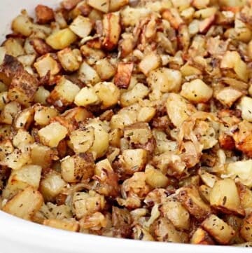 Close-up of roasted breakfast potatoes, diced and mixed with spices and herbs for a golden-brown, crispy texture. The flavorful potatoes are served in a white baking dish.