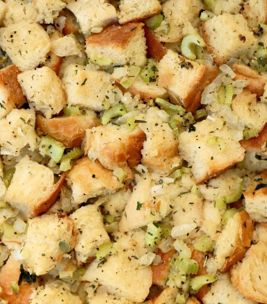 Cubed bread stuffing mixed with chopped celery, onions, and herbs, showing a close-up of the seasoned bread pieces and vegetable bits before baking.