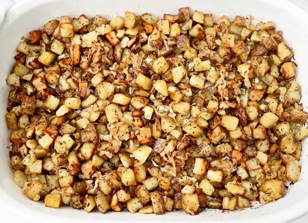 A baking dish filled with golden-brown roasted breakfast potatoes mixed with caramelized onions and sprinkled with herbs.