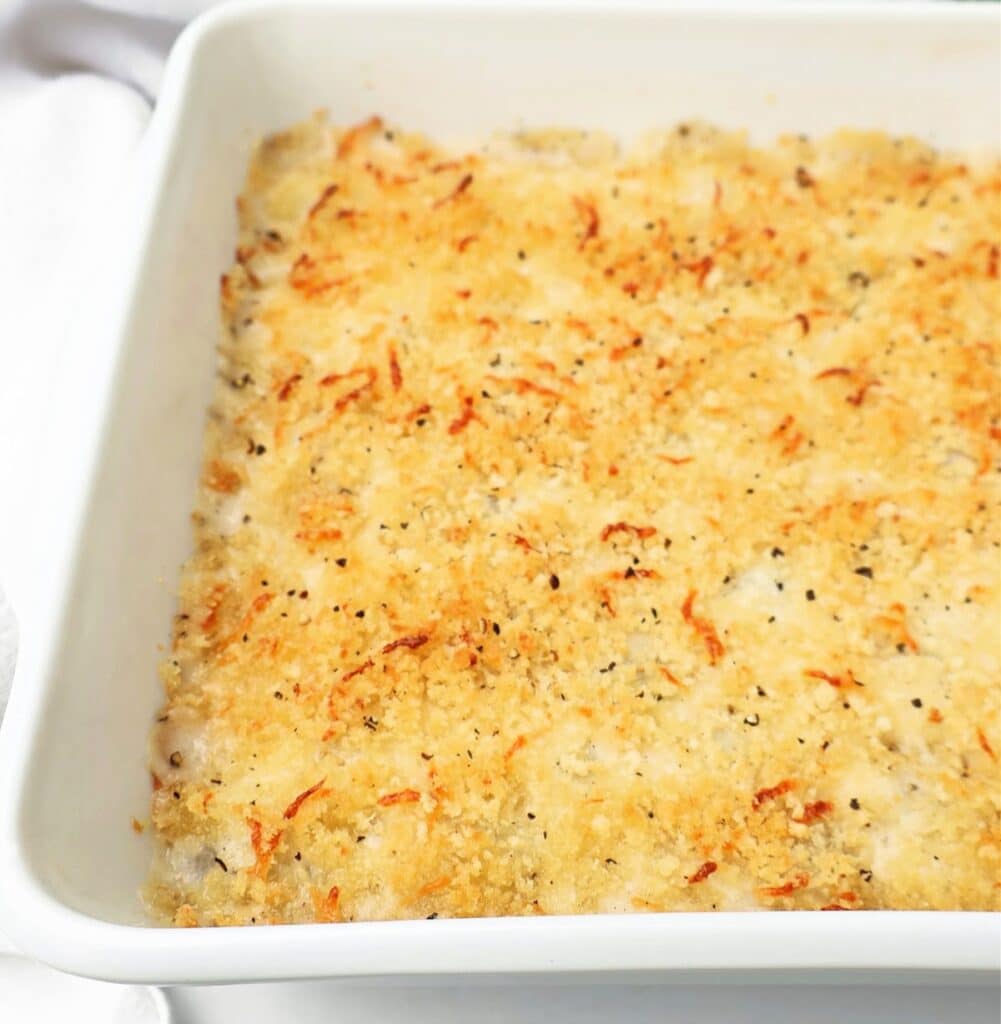 A close-up of a baked casserole featuring creamed onions, with a golden-brown, crispy breadcrumb and cheese topping in a white square baking dish.