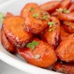 Close-up of balsamic roasted carrots glazed with a shiny coating, garnished with small sprigs of fresh green herbs, served in a white dish.