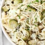 Roasted vegetable pasta salad featuring pasta topped with roasted Brussels sprouts, cauliflower, shredded Parmesan cheese, and chopped fresh herbs, served in a white bowl.