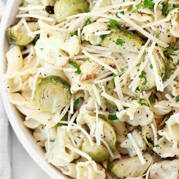 Roasted vegetable pasta salad featuring pasta topped with roasted Brussels sprouts, cauliflower, shredded Parmesan cheese, and chopped fresh herbs, served in a white bowl.