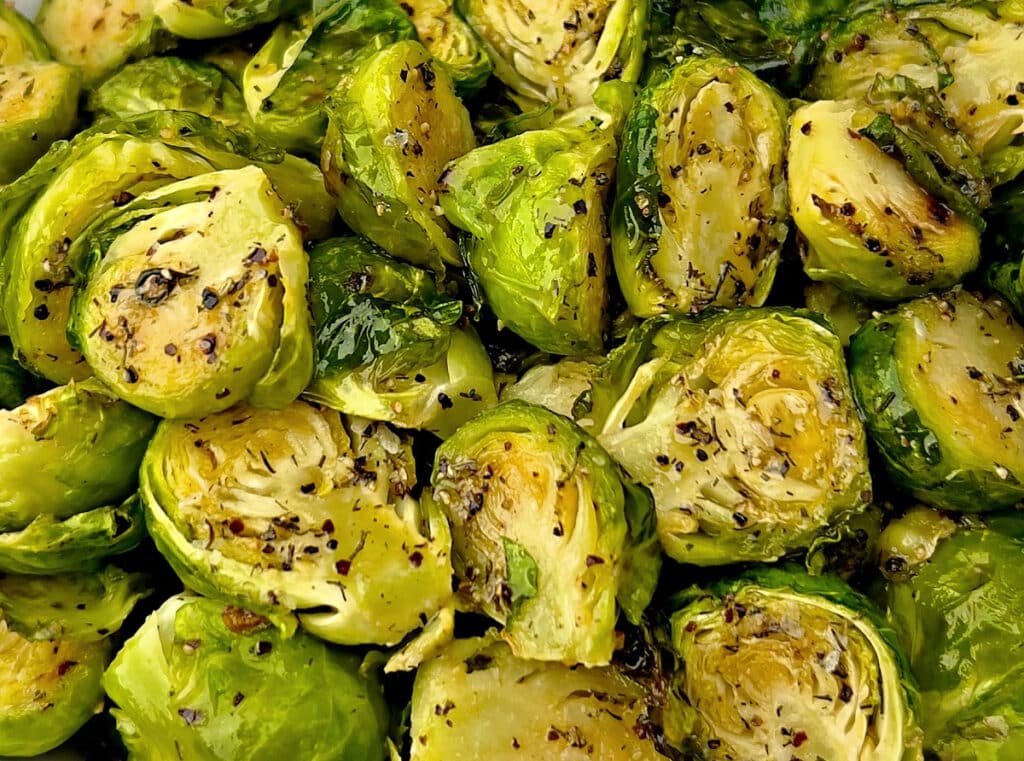 Close-up of roasted Brussels sprouts, halved and seasoned with cracked black pepper and herbs, displaying a golden-brown, crispy texture.
