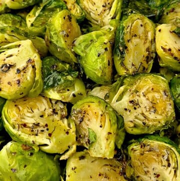 Close-up of roasted Brussels sprouts, halved and seasoned with cracked black pepper and herbs, displaying a golden-brown, crispy texture.