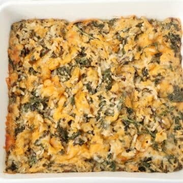 A white baking dish filled with a baked casserole made of rice, cheese, and leafy greens. The casserole has a golden-brown top with visible bits of melted cheese and green herbs mixed throughout.