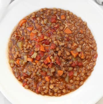 A bowl of lentil soup with diced carrots, celery, tomatoes, and lentils in a rich broth, served in a white bowl.