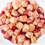 A bowl filled with golden-brown tofu cubes coated in a red, glossy sauce with pieces of what appears to be dried cranberries or fruit.