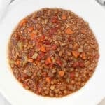 A bowl of lentil soup with diced carrots, celery, tomatoes, and lentils in a rich broth, served in a white bowl.