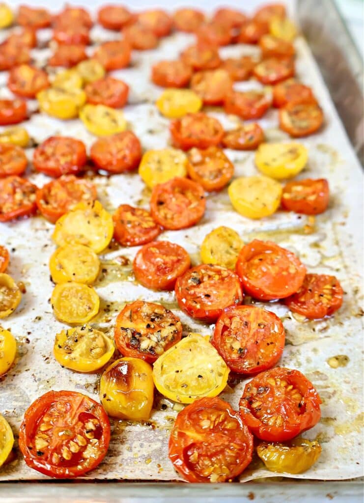 Sliced red and yellow cherry tomatoes, seasoned with herbs and spices, roasted on a parchment-lined baking sheet.