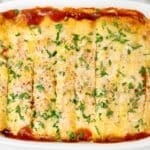 A baked dish of enchiladas topped with melted cheese and chopped cilantro, arranged in a white casserole dish with visible red sauce around the edges.