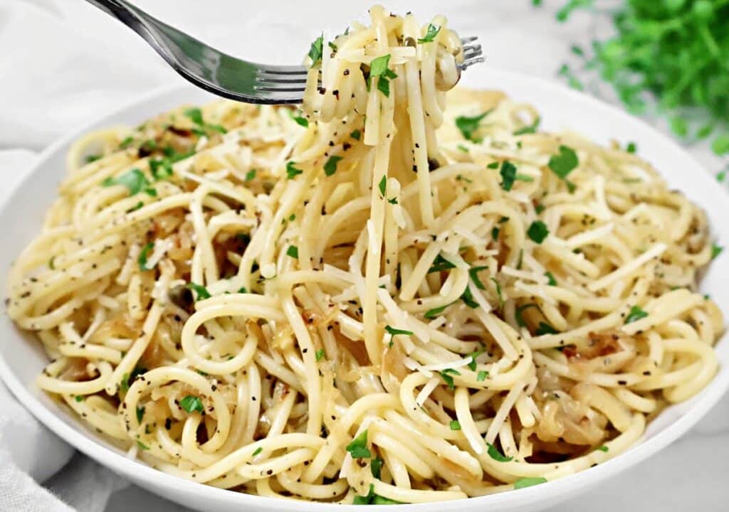 A fork lifts a serving of spaghetti from a bowl filled with pasta, garnished with chopped parsley, grated cheese, and ground black pepper.