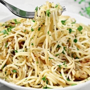 A fork lifts a serving of spaghetti from a bowl filled with pasta, garnished with chopped parsley, grated cheese, and ground black pepper.