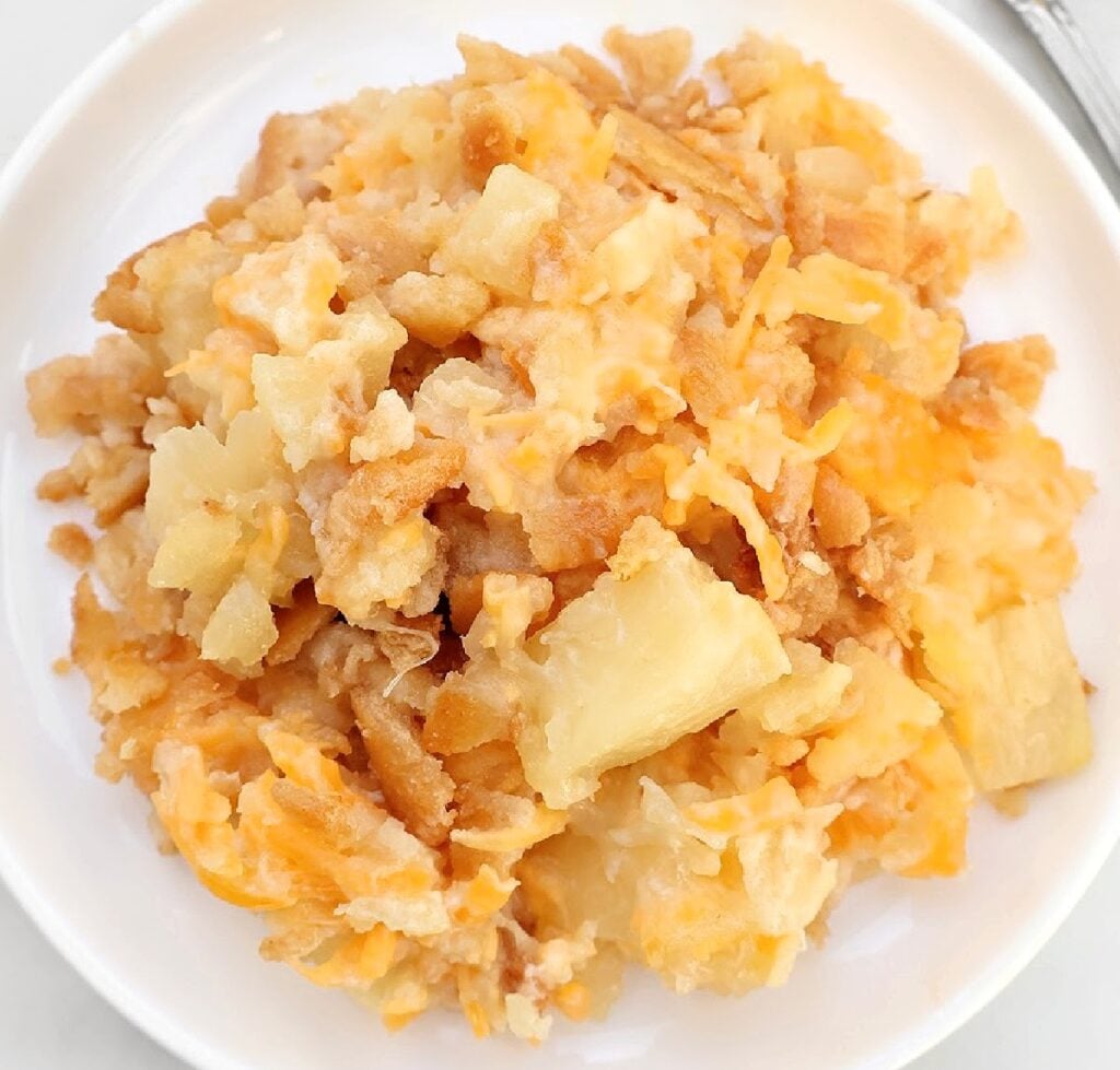 A serving of cheesy hashbrown casserole with chunks of potatoes and melted cheese on a white plate—a true favorite among Southern side dish recipes.