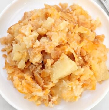 A serving of cheesy hashbrown casserole with chunks of potatoes and melted cheese on a white plate—a true favorite among Southern side dish recipes.