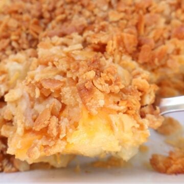 A close-up of a cheesy Southern side dish casserole, topped with a golden, crispy cracker and breadcrumb crust, with melted cheese and potato chunks visible underneath—perfect for those who love classic pineapple casserole flavors.