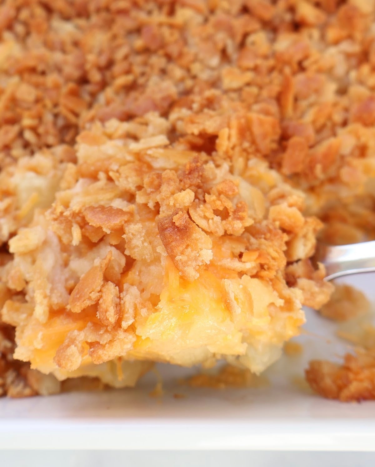 A close-up of a cheesy Southern side dish casserole, topped with a golden, crispy cracker and breadcrumb crust, with melted cheese and potato chunks visible underneath—perfect for those who love classic pineapple casserole flavors.