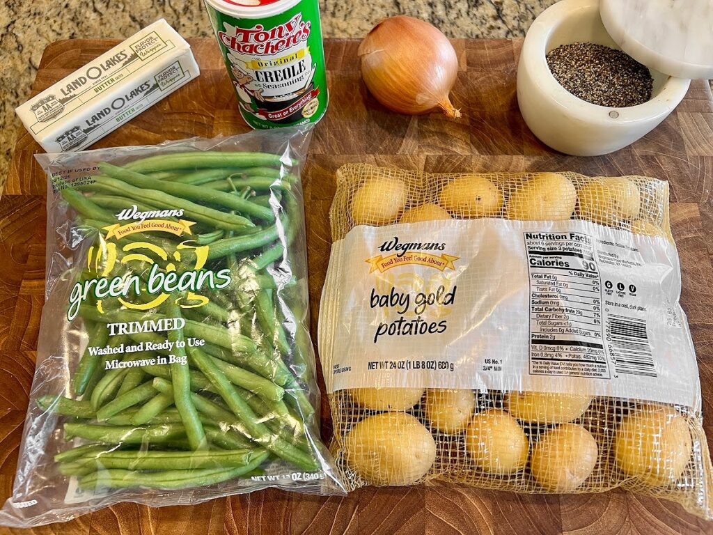 A bag of trimmed green beans, baby gold potatoes, butter, Creole seasoning, and ground black pepper are arranged on a wooden surface—perfect ingredients for a classic Southern green beans recipe or slow cooker green beans and potatoes.