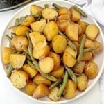 A white plate filled with halved baby potatoes and green beans, seasoned with black pepper and herbs. The vegetables appear cooked and lightly glazed, resembling a classic Southern green beans recipe.
