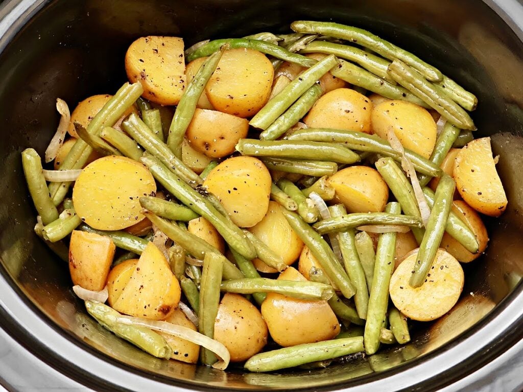 Sliced baby potatoes and fresh green beans, seasoned with pepper, are mixed together and cooked in a stainless steel pot for a classic Southern green beans recipe.
