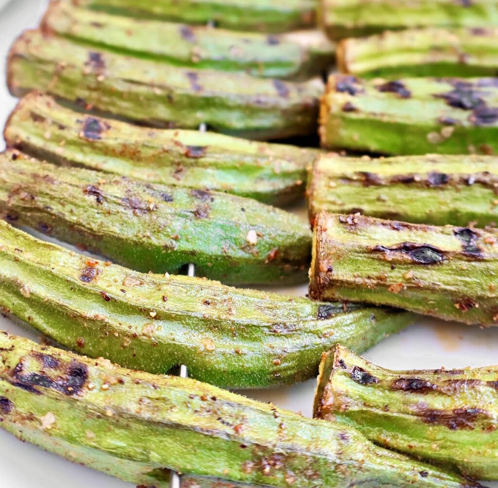 Smoky Grilled Okra pods seasoned with spices, arranged in rows on a white plate. The okra has visible grill marks and a slightly crispy texture, making this a perfect Southern okra recipe.