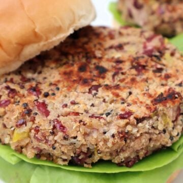 A close-up of a veggie burger patty on a leaf of lettuce, served in a soft bun. The patty has a textured, grainy appearance with visible bits of vegetables and grains.
