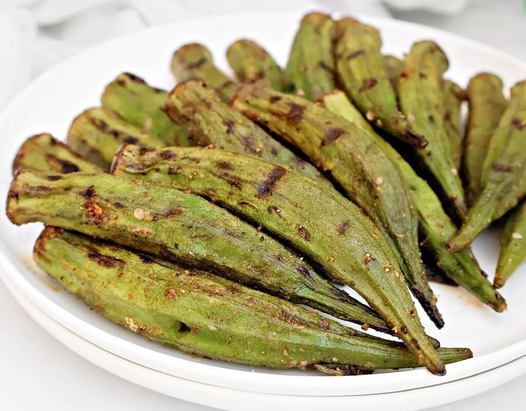 A white plate filled with Smoky Grilled Okra, featuring char marks and seasoning on the green pods—a classic Southern okra recipe perfect for summer gatherings.