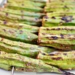Close-up of Smoky Grilled Okra skewers, showing green okra pods with slight char marks and a coating of spices. Perfect for a Southern okra recipe, the rows of skewers highlight the okra’s texture and rich, smoky flavor.