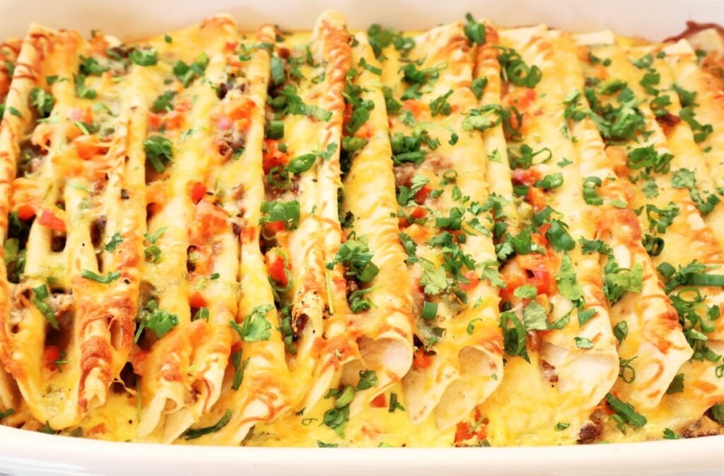 A close-up of an easy Mexican breakfast casserole, filled with cheesy enchiladas, topped with melted cheese, chopped tomatoes, and fresh cilantro.