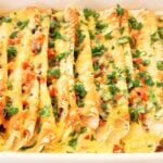A close-up of an easy Mexican breakfast casserole, filled with cheesy enchiladas, topped with melted cheese, chopped tomatoes, and fresh cilantro.