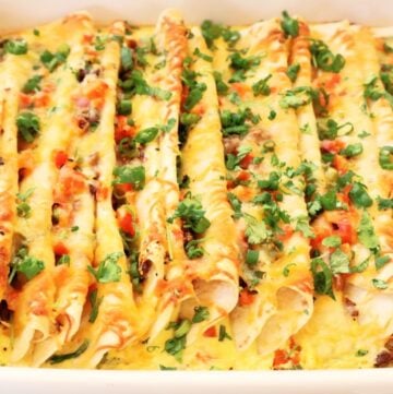 A close-up of an easy Mexican breakfast casserole, filled with cheesy enchiladas, topped with melted cheese, chopped tomatoes, and fresh cilantro.