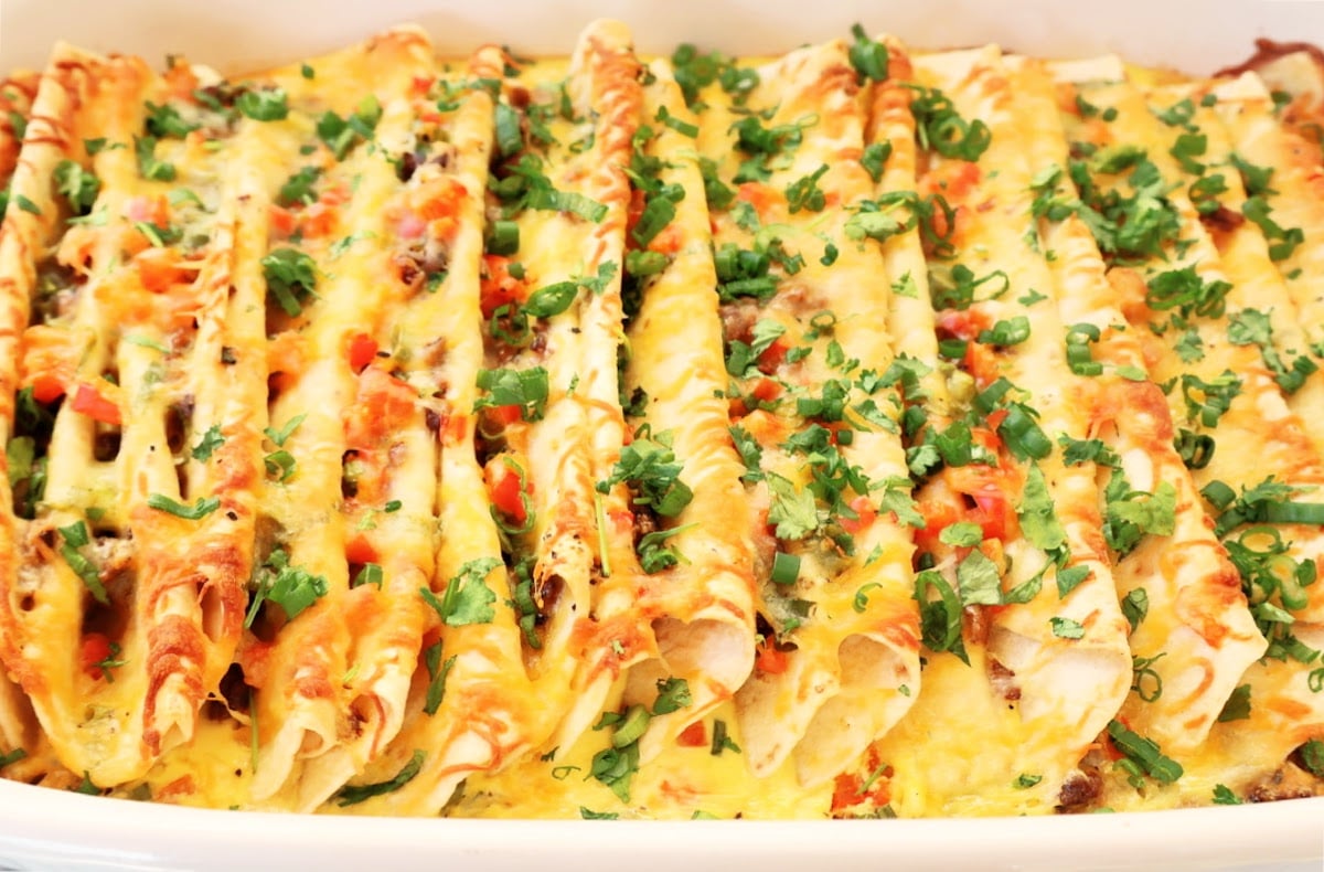 A close-up of an easy Mexican breakfast casserole, filled with cheesy enchiladas, topped with melted cheese, chopped tomatoes, and fresh cilantro.