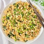 A bowl of cooked bok choy ramen noodles topped with chopped green onions, peanuts, and leafy greens, with a pair of brown chopsticks resting on the side of the bowl.