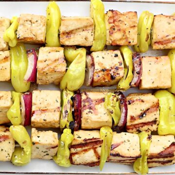 Three grilled skewers with cubed Mississippi Tofu, yellow pepper slices, and red onion pieces, arranged neatly on a white platter. The tofu is lightly charred, and the vegetables are bright and fresh-looking.