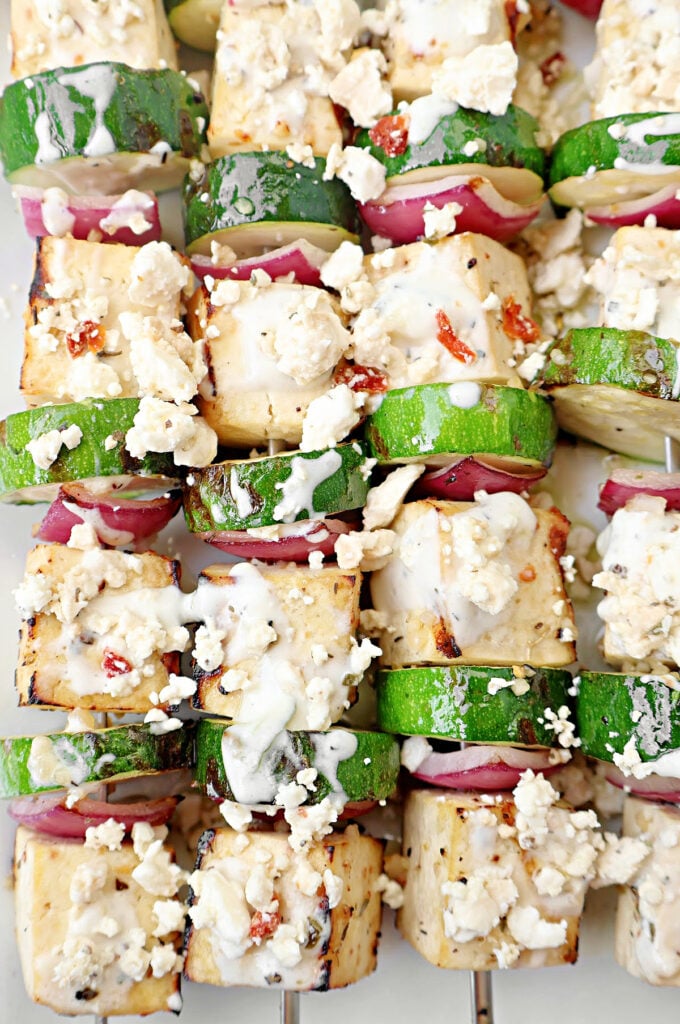 Skewers with grilled tofu, zucchini slices, and red onion, topped with crumbled feta cheese and a light drizzle of creamy sauce—this tofu souvlaki is a fresh twist on a classic Greek favorite.