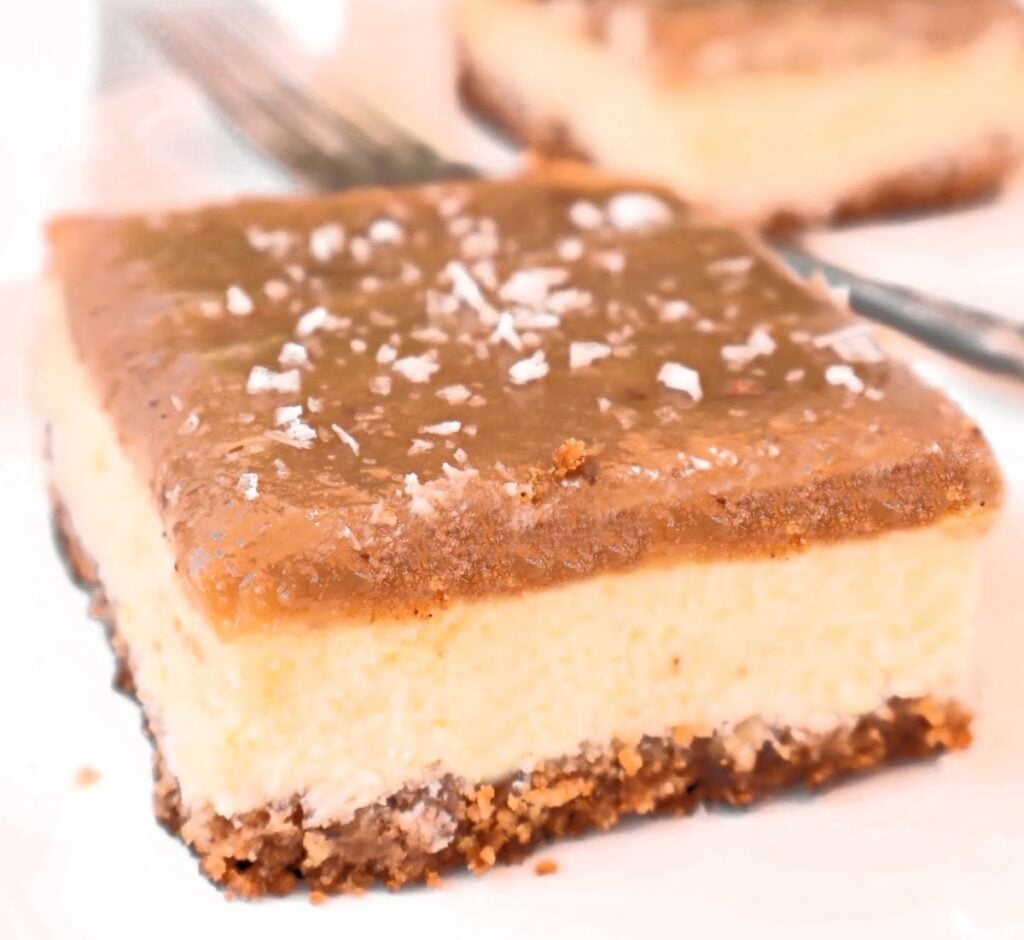 A close-up of Salted Caramel Cheesecake Bars with a crumbly base, creamy middle layer, and caramel-like top, all sprinkled with coarse sea salt.